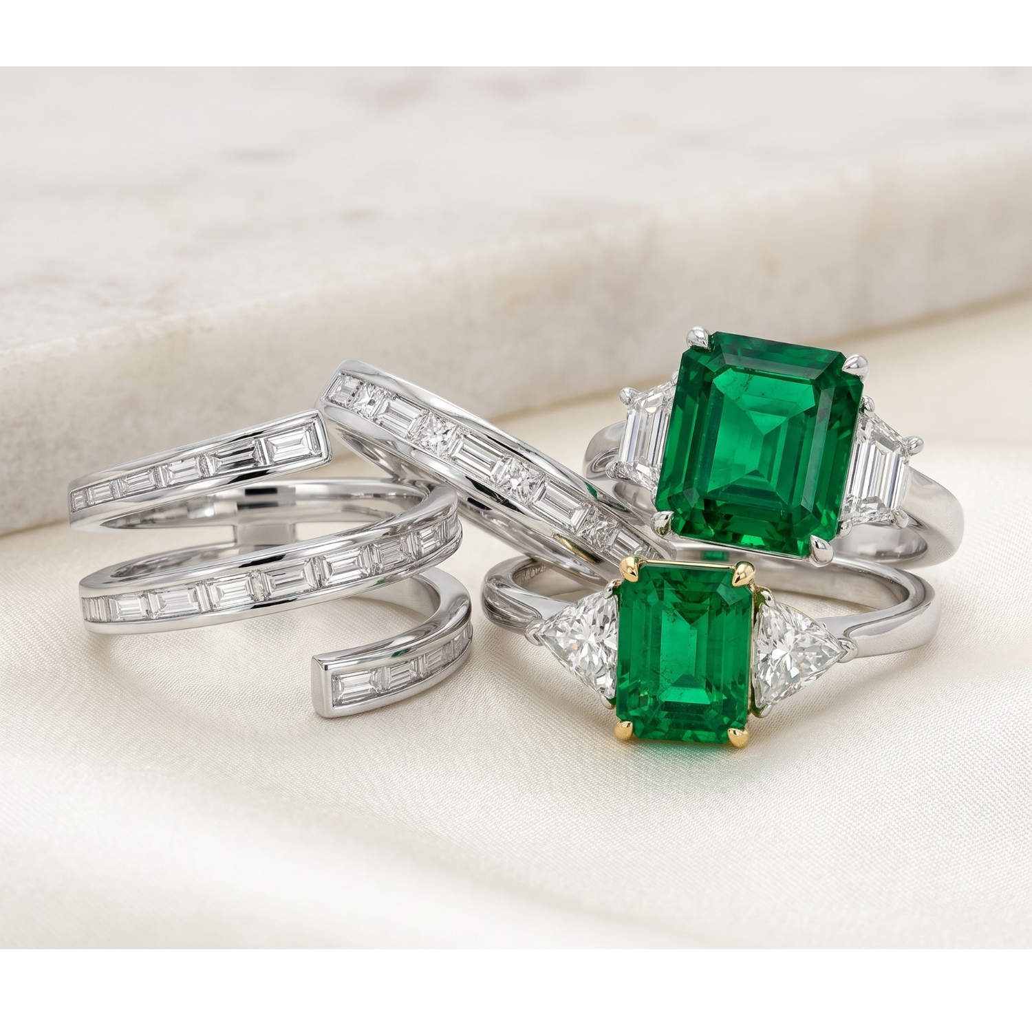 Two emerald-cut gemstone rings with diamond accents on a light background